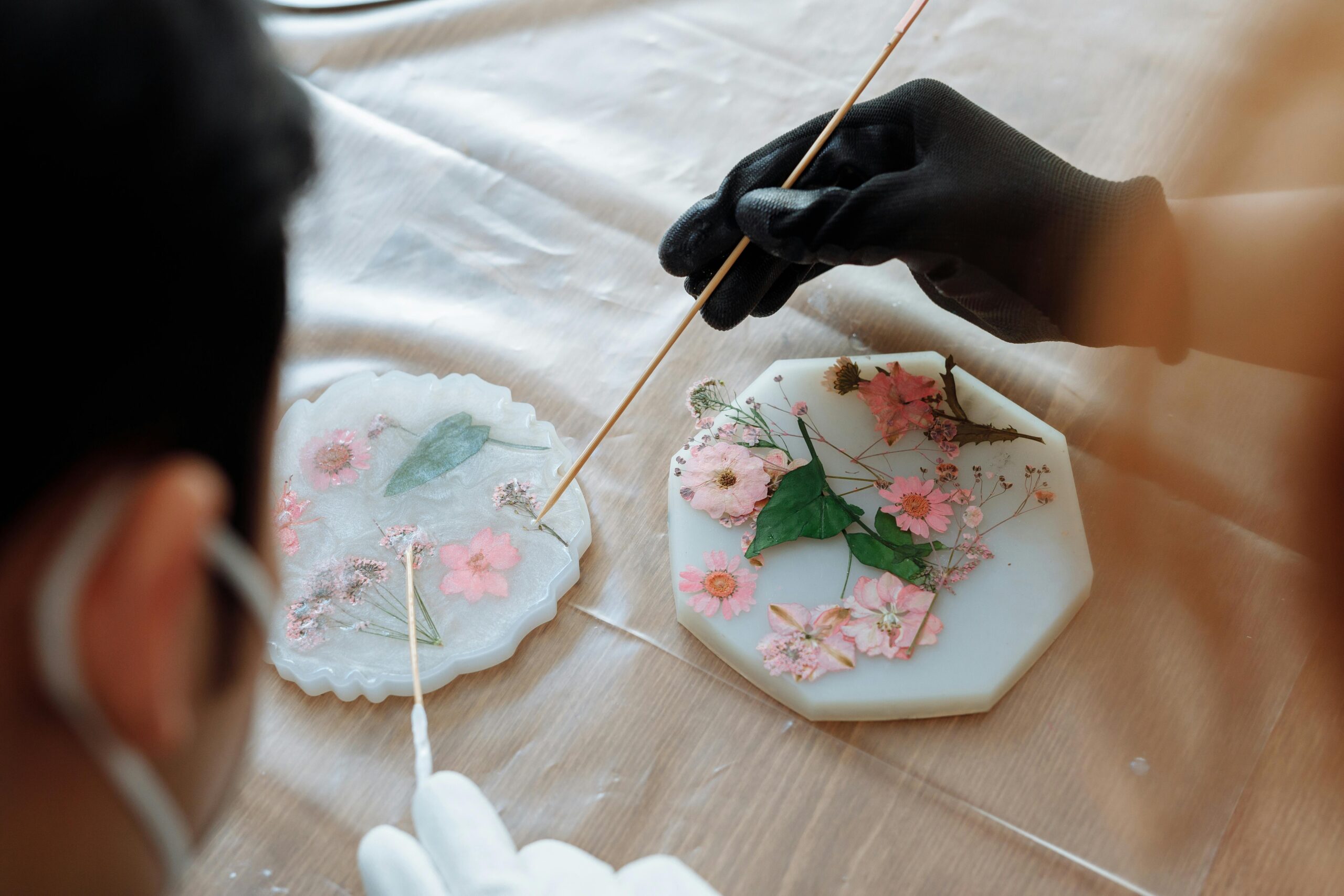 Close-up of hands arranging dried flowers in resin molds for decorative art.